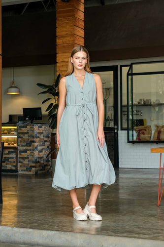Woman wearing a light blue dress standing in an indoor setting with wooden beams and a counter.